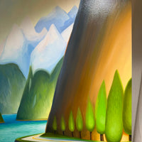 A stylized landscape artwork showing a winding road beside a turquoise lake, green trees, layered mountains, and a large dark cliff face lit by warm golden light.